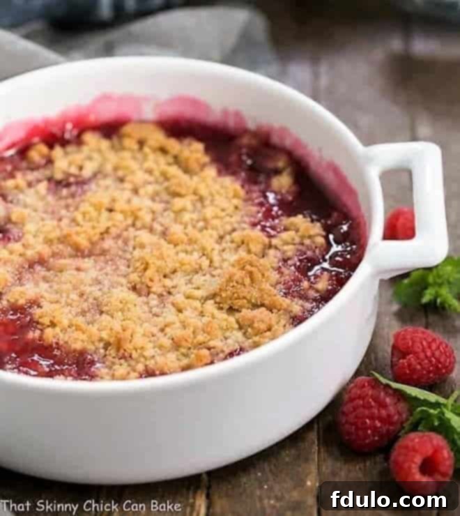 A warm Fresh Raspberry Crisp beautifully presented in a round white casserole dish, showcasing its golden-brown topping and vibrant fruit filling.
