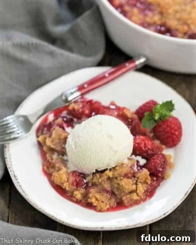 An overhead view of Fresh Raspberry Crisp served on a white dessert plate, accompanied by a scoop of melting vanilla ice cream and garnished with fresh raspberries.