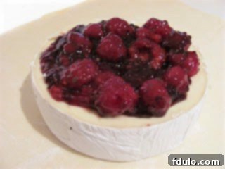 Brie with berry topping on a sheet of parchment, ready to be wrapped.