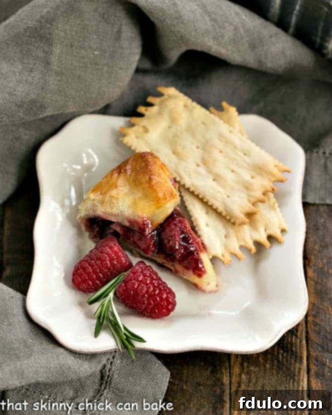 Slice of raspberry brie en croute on an appetizer plate with crackers and fresh raspberries, ready to be enjoyed.