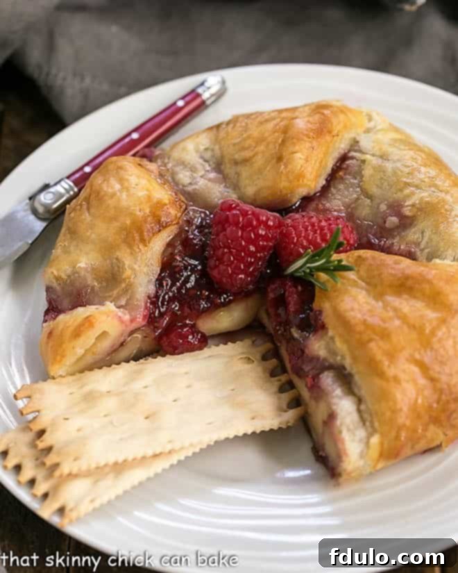 Raspberry Brie en Croute on a serving plate with crackers and a red handled knife, ready to be sliced.