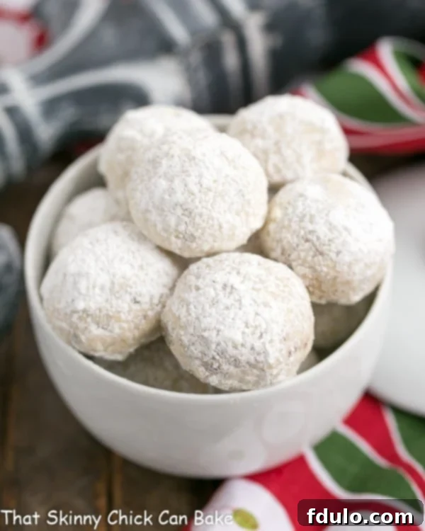 A round white bowl filled with freshly baked and powdered Pecan Snowballs, ready for holiday festivities.