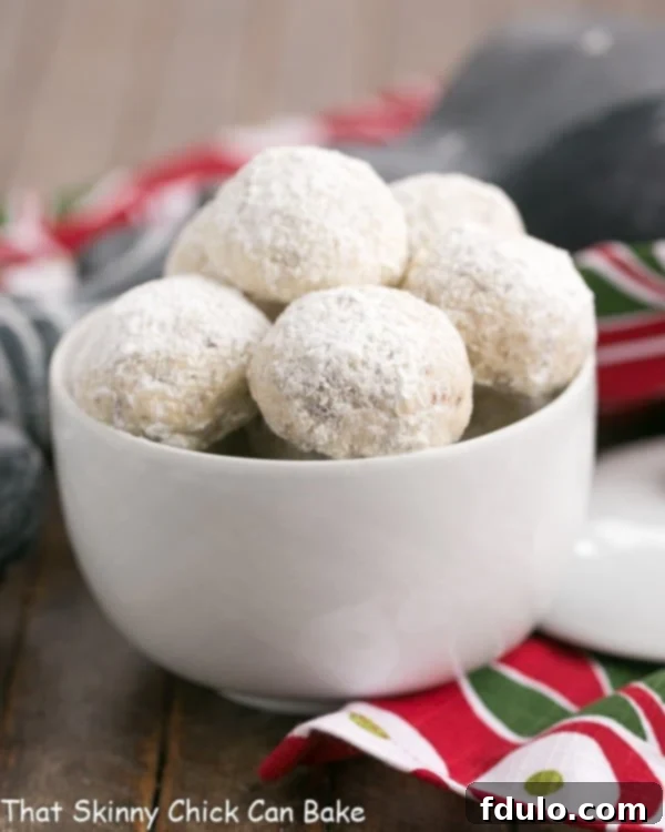 A close-up shot of Pecan Snowballs elegantly arranged in a white ceramic bowl, showcasing their delicate powdered sugar coating.