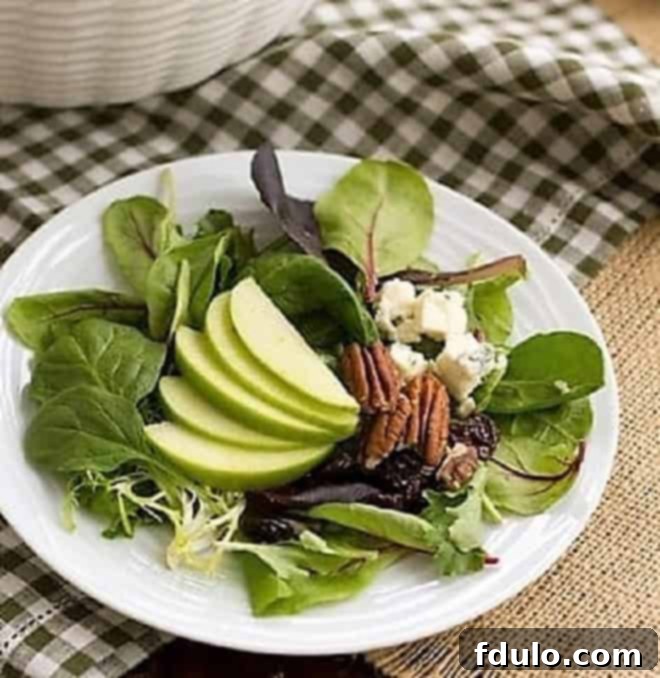 A close-up view of a serving of Winter Salad with Apples, Pecans, Blue Cheese and Dried Cherries on a small white plate, highlighting the fresh ingredients and vibrant colors.