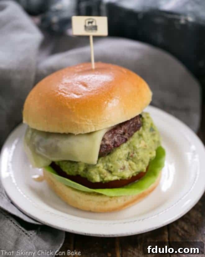 Grilled Guacamole Burger - a grilled beef hamburger topped with melted Monterey jack cheese and a creamy mound of guacamole A perfectly assembled Grilled Guacamole Burger on a clean white plate, ready to be enjoyed. The melted cheese and creamy guacamole are prominently displayed.