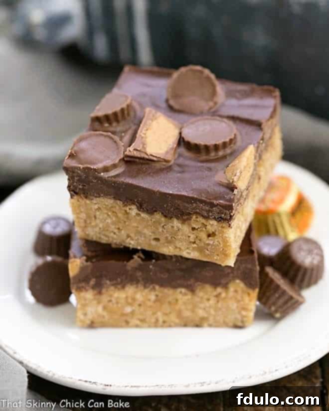A stack of golden brown Reese's Rice Krispie Treats topped with chocolate and miniature Reese's peanut butter cups, presented on a small white ceramic plate.