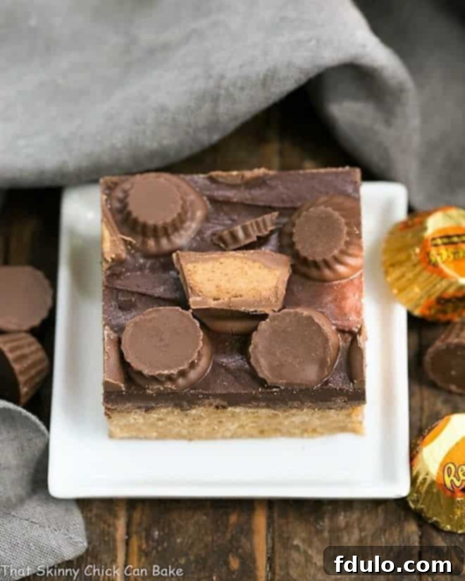 Three perfectly cut Reese's Rice Krispie Treats, featuring a crispy peanut butter base and a smooth chocolate topping with mini peanut butter cups, on a small white square ceramic plate.