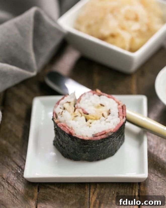 Beefshi - Reuben Rolls are a fun twist on classic sushi made with deli corned beef, sushi rice, sauerkraut and Swiss Cheese Beefshi - Reuben Roll on a small white square plate, ready to be enjoyed