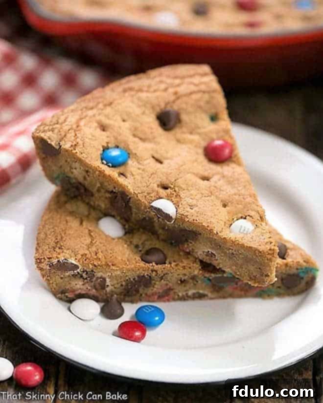 Patriotic Skillet Cookie wedges stacked on a white enamel dessert plate, showcasing the vibrant red, white, and blue M&M's and melted chocolate chips.