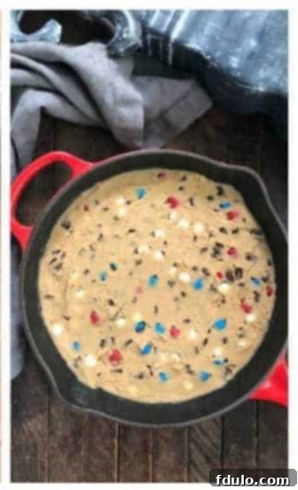 Cookie dough being spread evenly into a greased red cast iron skillet with an offset spatula.