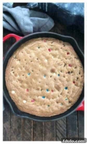 A golden brown Patriotic Skillet Cookie baking in a red cast iron skillet in the oven.