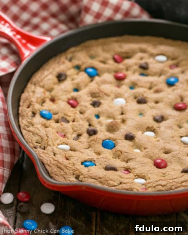 A perfectly baked Patriotic Skillet Cookie, garnished with extra M&M's and chocolate chips, resting in a red cast iron skillet.