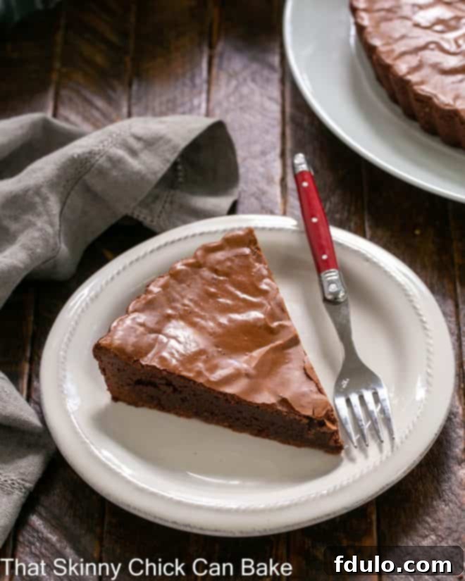 Ungarnished slice of brownie pie on a white dessert plate with a red handled fork.