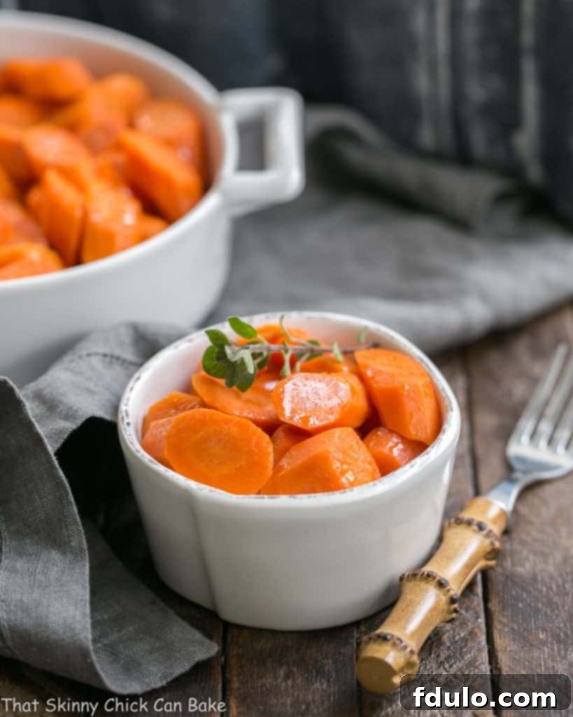 Bourbon Maple Glazed Carrots - An easy way to transform carrots into a restaurant worthy side dish! A small white bowl filled with glistening Bourbon Maple Glazed Carrots, garnished with a fresh herb, next to a bamboo fork.