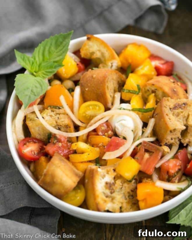 A vibrant Summer Tomato and Burrata Panzanella Salad in a pristine white serving bowl, garnished with fresh basil leaves.