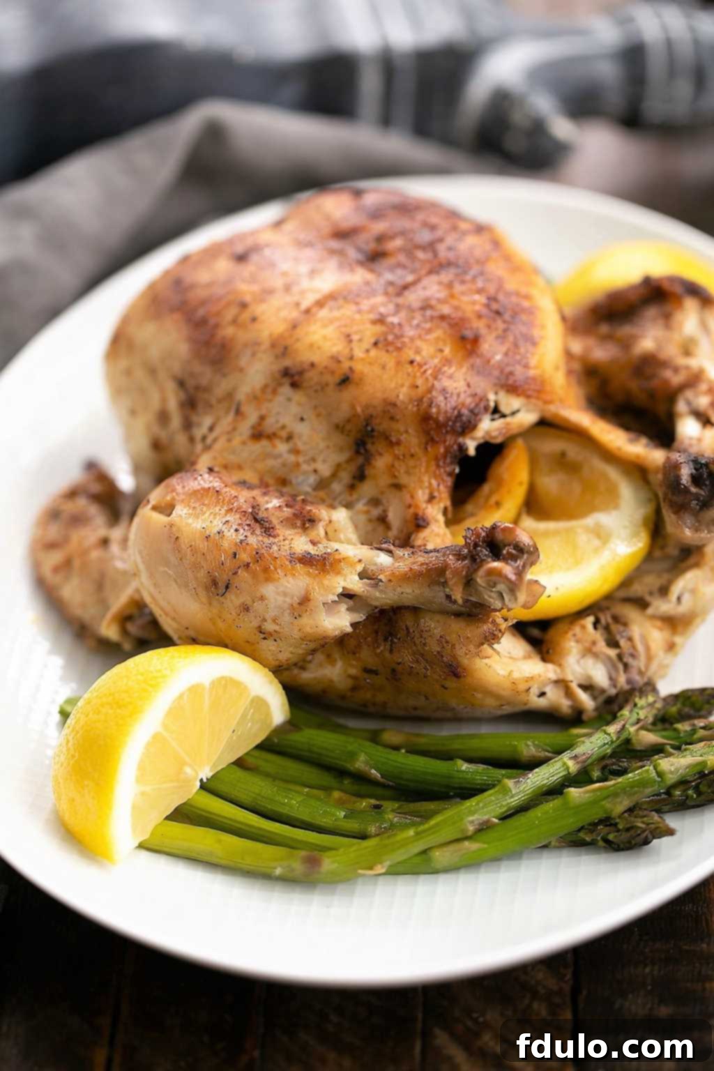 Whole Instant Pot Rotisserie Chicken on a white platter with fresh lemon wedges and herbs.