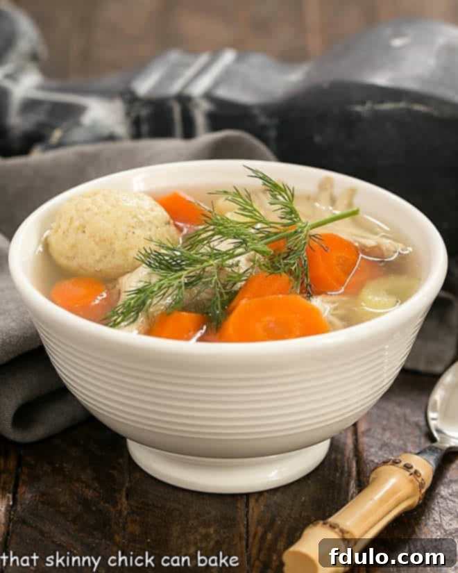 Side view of Matzo Ball soup in a white bowl with fresh dill garnish.