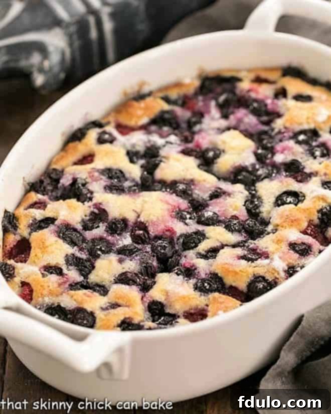 Mixed berry cobbler in a white, oval casserole dish, showing the golden brown topping and bubbling fruit underneath.