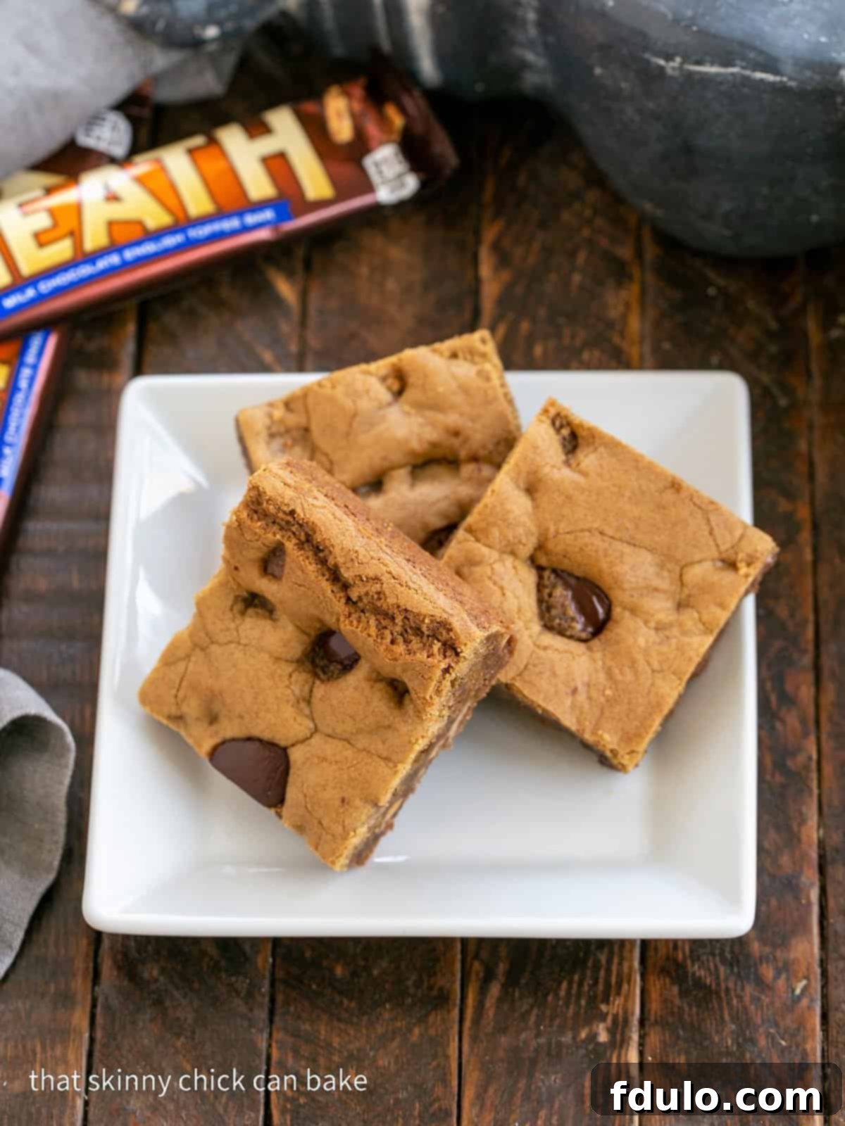 Three perfectly cut Toffee Blondies artfully arranged on a square white plate, highlighting their delightful texture and the visible chunks of toffee.