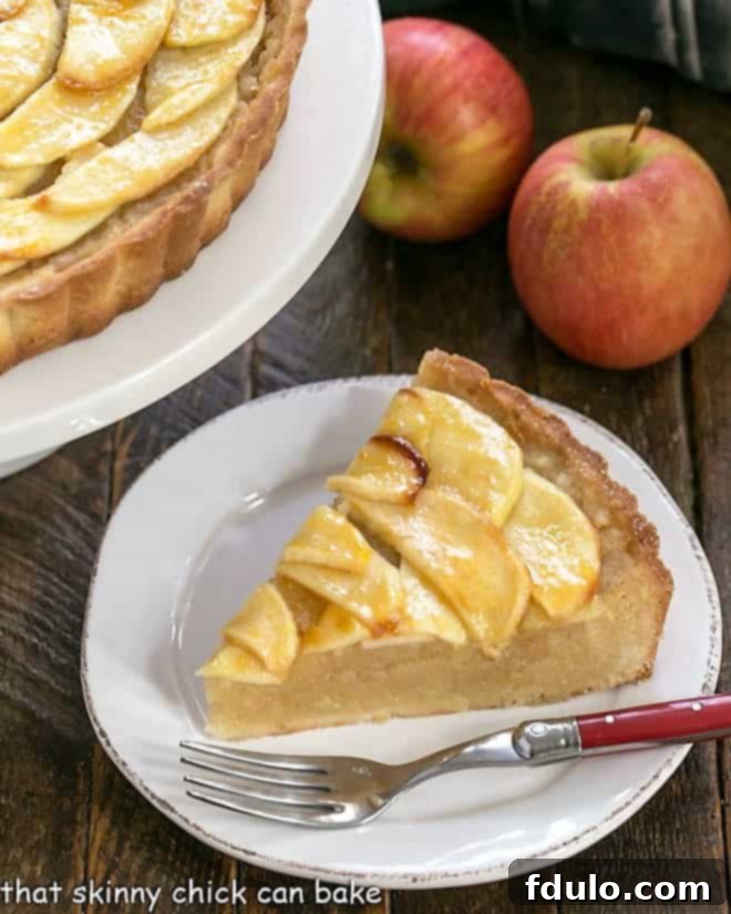 A slice of French Apple Tart on a white plate with a red-handled fork, showcasing its layers