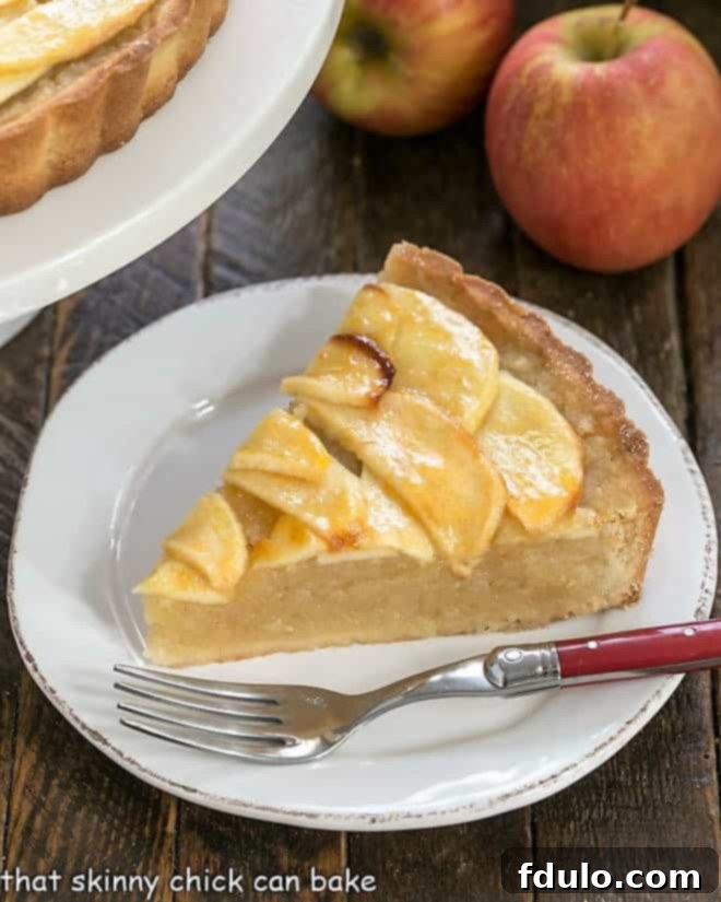 Slice of French apple tart on a round white plate, showing the buttery crust and apple layers