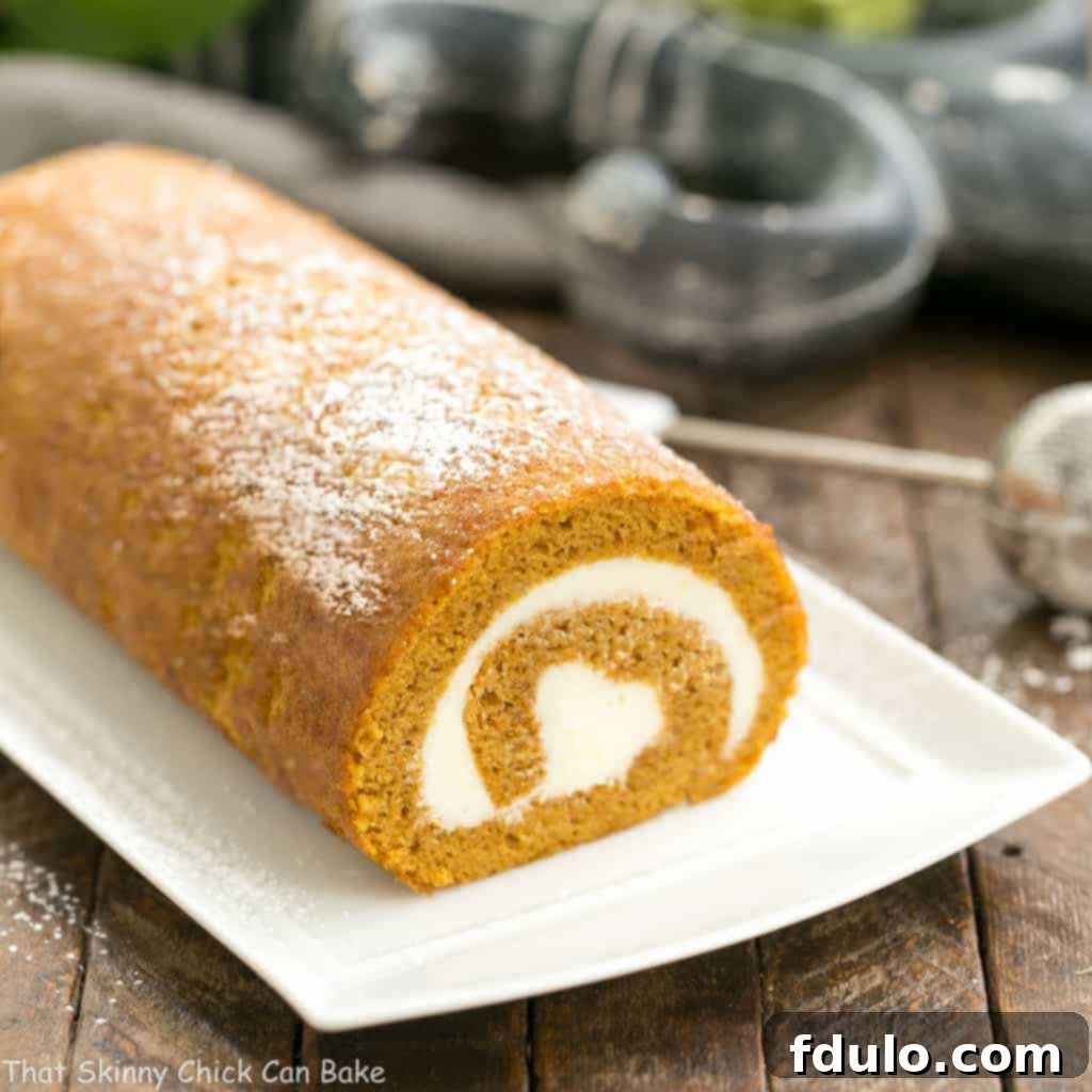 A beautifully rolled Pumpkin Roll, sliced to reveal the swirl of cream cheese filling.