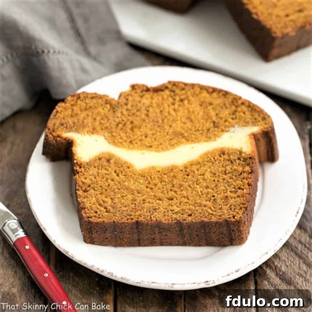 Moist Pumpkin Bread filled with a creamy ribbon of cream cheese, sliced to show the filling.