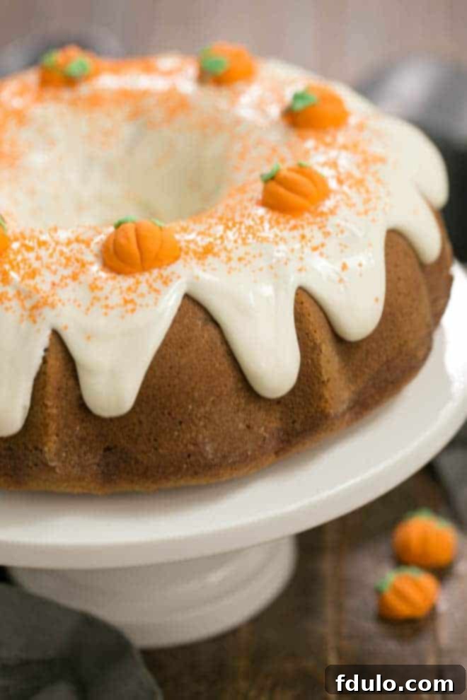 A stunning Pumpkin Spice Bundt Cake on a white ceramic cake stand, showcasing a generous crown of cream cheese frosting.