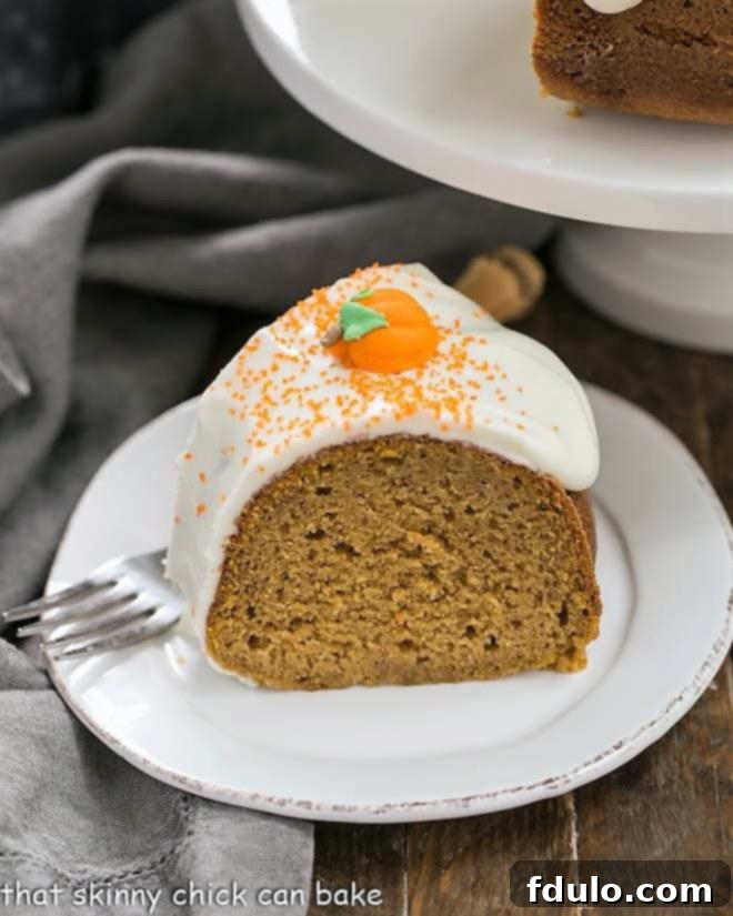 A perfectly sliced piece of Pumpkin Spice Bundt Cake resting on a white dessert plate, revealing its moist interior and rich frosting.