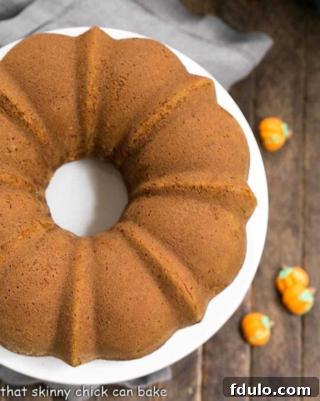 A beautifully presented Pumpkin Spice Bundt Cake on a white cake plate, ready to be served, highlighting its intricate design and frosting.