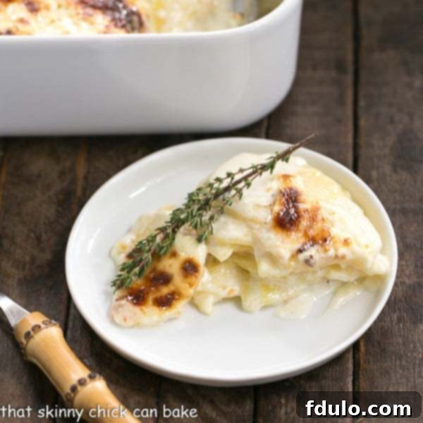 French Potato Gratin - An exquisite creamy cheesy potato casserole kissed with garlic, thyme and topped with Gruyere cheese, perfect for any special occasion. A perfectly portioned serving of French Potato Gratin on a round white plate, ready to be enjoyed with a bamboo-handled fork, highlighting its creamy layers and golden crust.