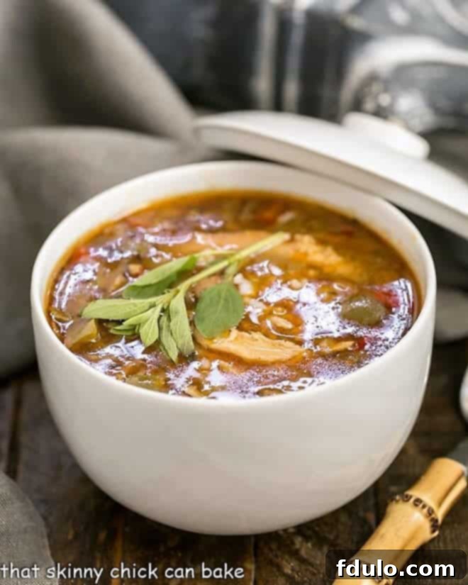 A steaming bowl of Sausage and Chicken Gumbo, garnished with fresh parsley, served with a bamboo spoon on a rustic wooden surface.