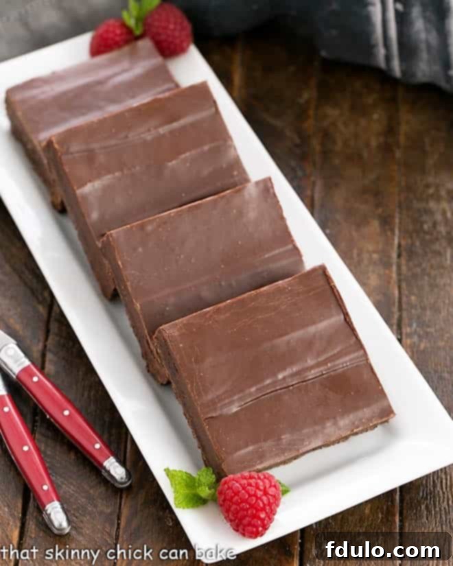 Decadent Fudge Topped Brownies, beautifully arranged on a white ceramic tray, garnished with fresh raspberries and vibrant mint leaves, showcasing their rich, dark chocolate appeal.