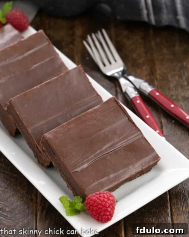 Perfectly cut fudge topped brownie squares, gleaming with glossy chocolate frosting, presented on a white serving platter, ready to be enjoyed.