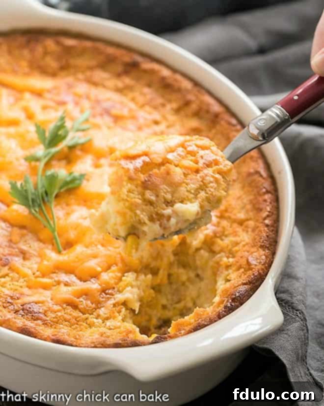 A spoonful of creamy corn pudding recipe on a red-handled serving spoon, showcasing its rich texture.