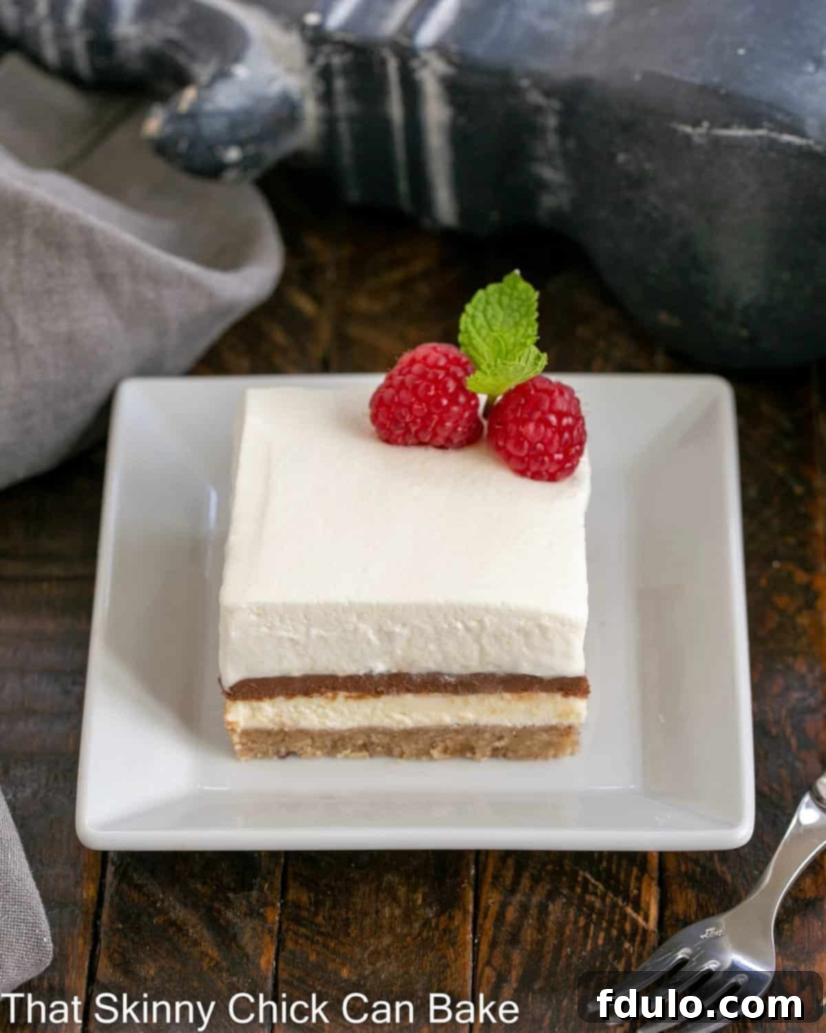 A square slice of homemade Chocolate Delight on a white plate, garnished with a fresh raspberry and a sprig of mint, showcasing its distinct layers.