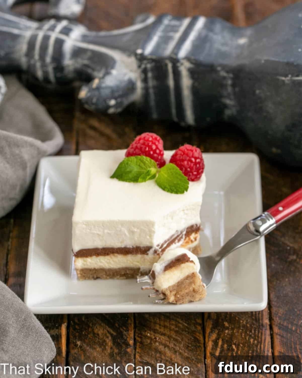 A square piece of Chocolate Delight on a white plate, with a red fork taking a bite, showing the rich, layered texture.