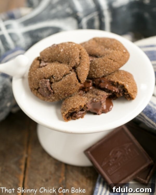 Chocolate Gingerbread Cookies on a small white pedestal, with one broken in half to reveal the melty chocolate interior