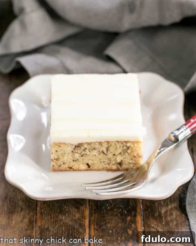 A beautifully frosted slice of Sour Cream Banana Cake on a square ceramic plate, ready to be enjoyed.