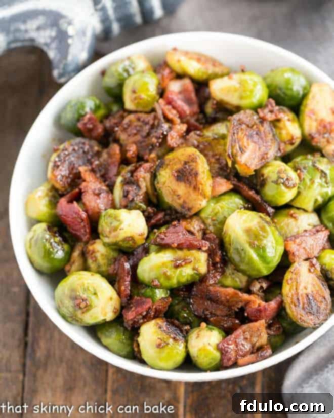 Close-up of Maple Syrup Mustard Glazed Brussels Sprouts with crispy bacon in a white serving bowl, showcasing their golden-brown char and glistening glaze.