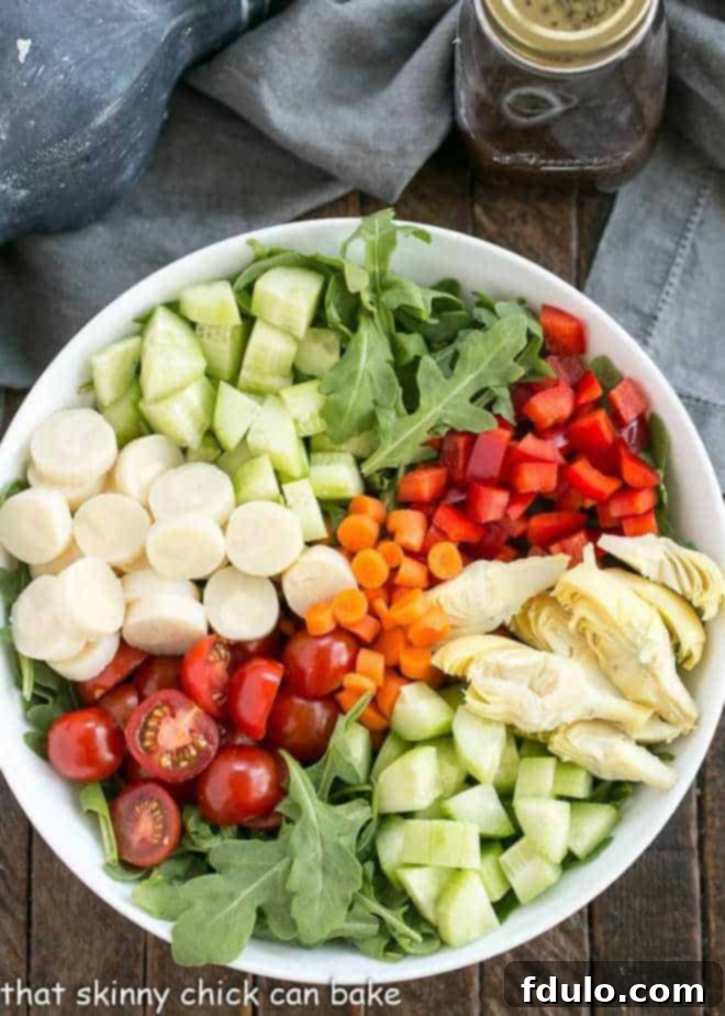 Arugula and chopped vegetable salad soon to be drizzled with a magnificent Easy Balsamic Vinaigrette Easy Balsamic Vinaigrette alongside a fresh vegetable salad in a white bowl, poised for dressing.