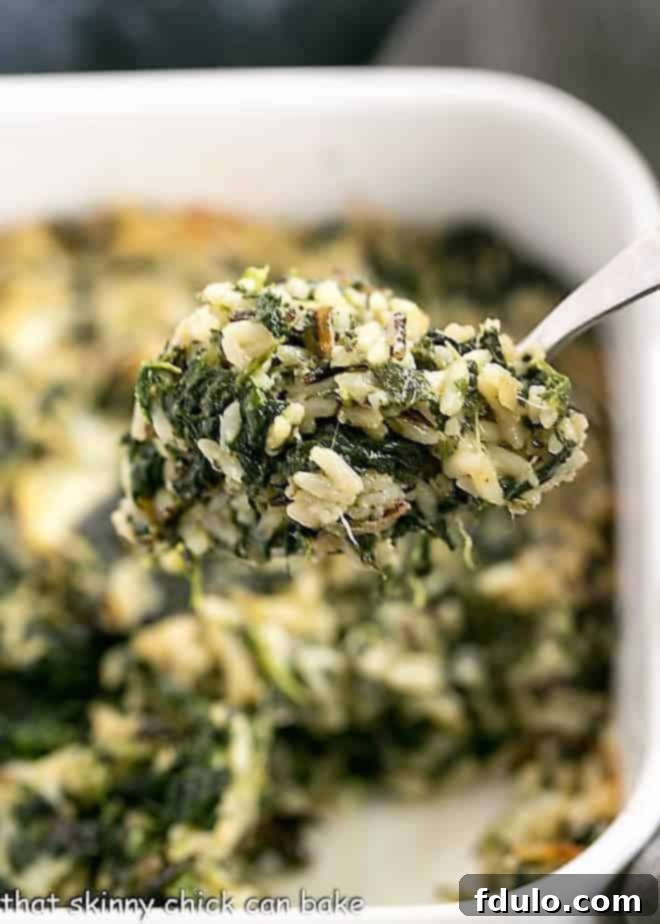 A generous spoonful of warm Cheesy Spinach Rice Casserole being lifted from a baking dish, showcasing its creamy texture and visible spinach.