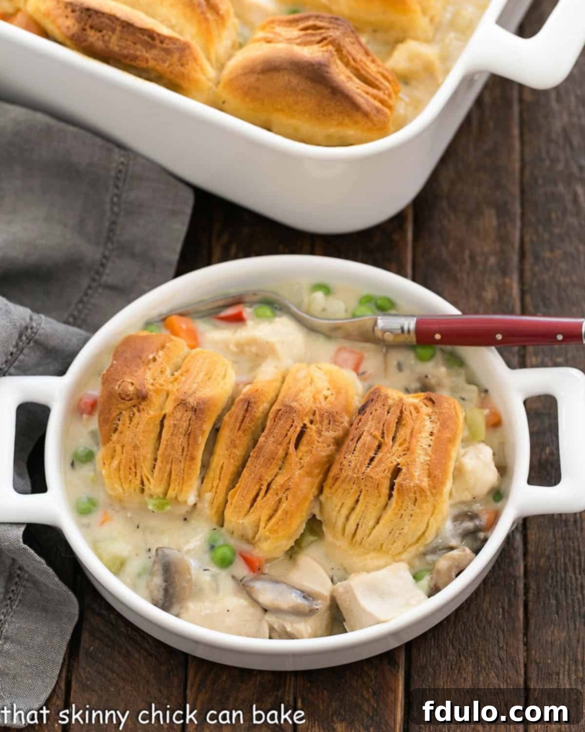 Homemade Chicken Pot Pie - comfort food at its finest topped with the flakiest, tender buttermilk biscuits Serving of chicken pot pie in a shallow dish with a red handled fork.