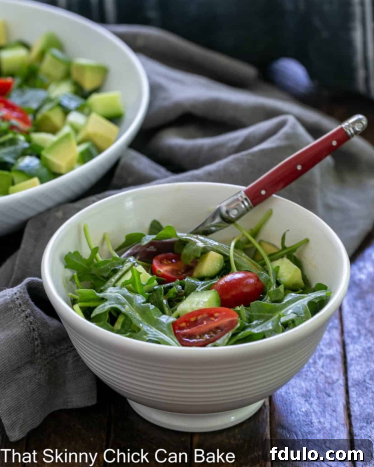 A vibrant salad bowl filled with fresh arugula salad, with a red-handled fork resting invitingly in front of the serving bowl.