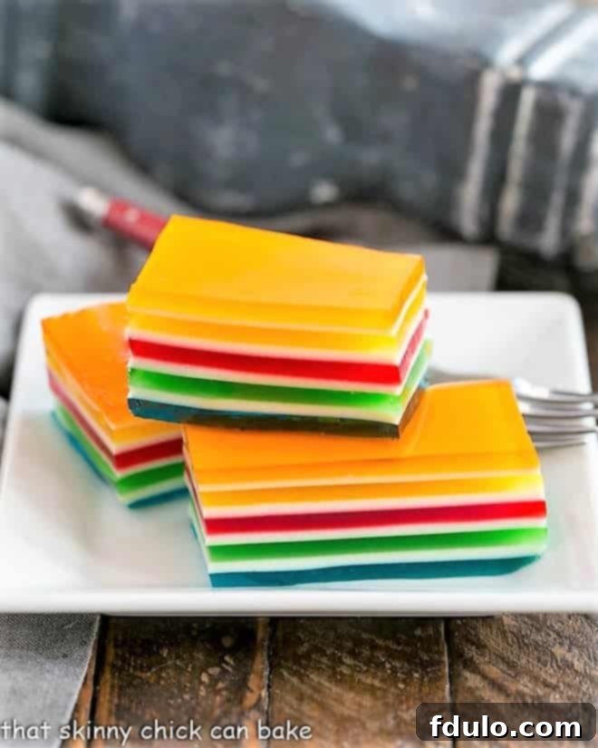 Layered Jello Rainbow Salad squares stacked on a white plate, showcasing vibrant colors.