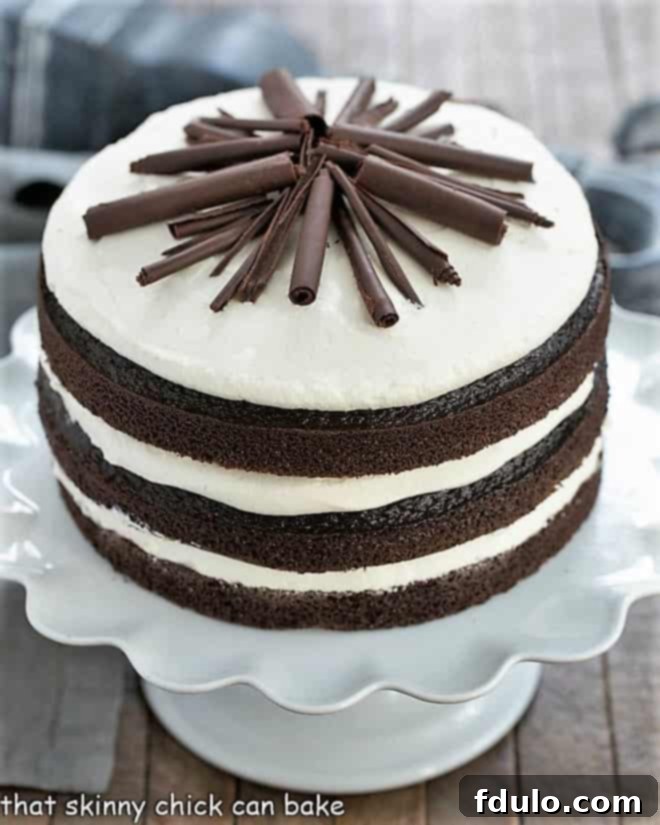 Triple Chocolate Layer Cake on a white cake stand, garnished with chocolate shavings.