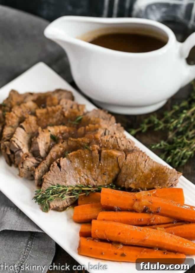 Braised Cola Brisket with Bourbon Gravy on a white platter with carrots and a pitcher of gravy.
