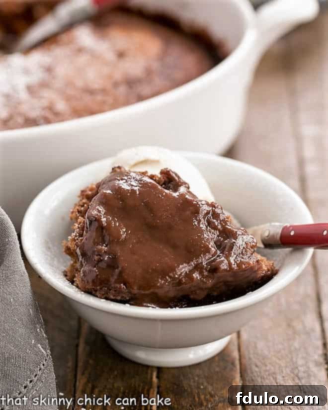 Easy Chocolate Pudding Cake - this Bisquick pudding cake is easy and bakes up into a soft cake layer and a fudgy sauce layer! Easy Chocolate Pudding Cake in a white bowl with a red handled fork, highlighting the self-saucing fudge layer.