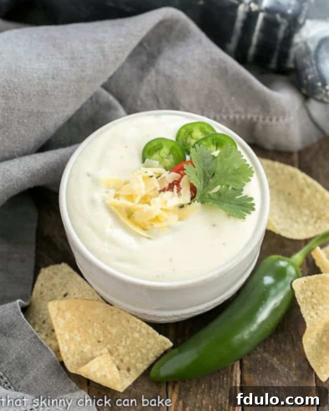 Small white bowl of Easy Homemade Queso Dip garnished with shredded cheese and cilantro, ready to be served.
