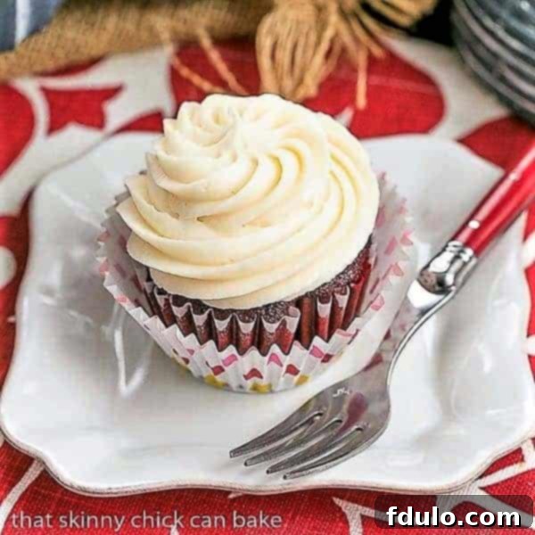 A close-up of a delectable Red Velvet Cupcake presented on a square white plate, accompanied by a charming red-handled fork, emphasizing its rich frosting and inviting texture.